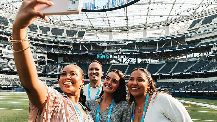 Tour group of three women and one man taking a selfie in SoFi Stadium