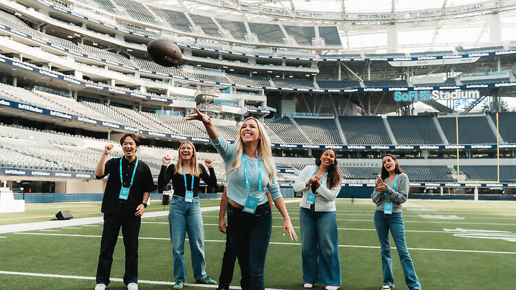 A woman throws a football in front of a small group of tour members on the field in SoFi Stadium