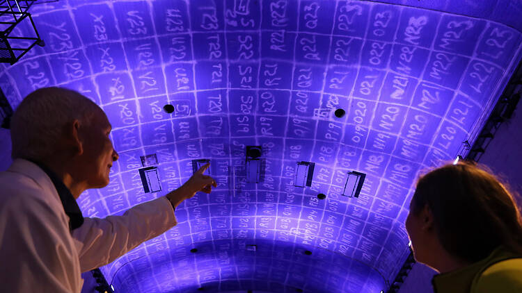 Stockholm, KTH reaktorhall, Open House Stockholm 2026 Two people in KTH's reactor hall, looking up at a purple-lit curved wall marked with a painted grid.