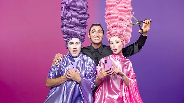 man dressed in black appears to cut pink wig with scissors, flanked by persons in purple and pink