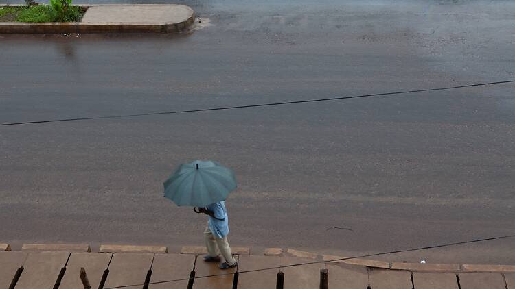 Man with green umbrella walking down a street during the rainy season in Sierra Leone Man with green umbrella walking down a street during the rainy season in Sierra Leone