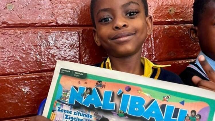 A South African learner holding a newspaper written Nalibali A South African learner holding a newspaper written Nalibali