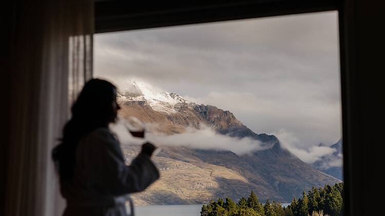 Guest enjoying wine while looking at hotel room view of mountainscape at voco Queenstown