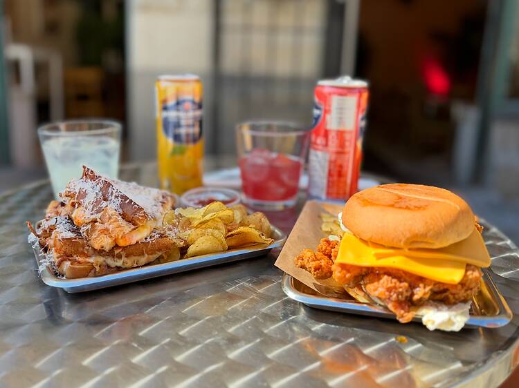 Stockholms Best Street Food: Sandwiches and Fried Chicken Burger at Sandhäxan in Vasastan, Stockholm A tray of loaded grilled cheese sandwiches with potato chips next to a fried chicken burger on a metal table outside Sandhäxan in Stockholm.