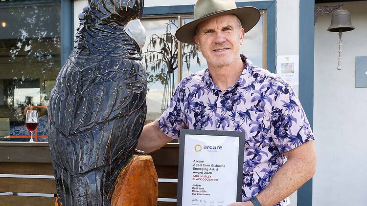 Artist Paul Hurley's Black Cockatoo sculpture man stands next to sculpture of black cockatoo