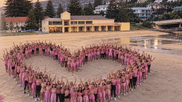 women wearing pink form a heart shape on the beach