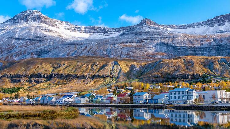 Colourful houses in front of a snowy mountain and behind a reflective lake in Iceland Colourful houses in front of a snowy mountain and behind a reflective lake in Iceland
