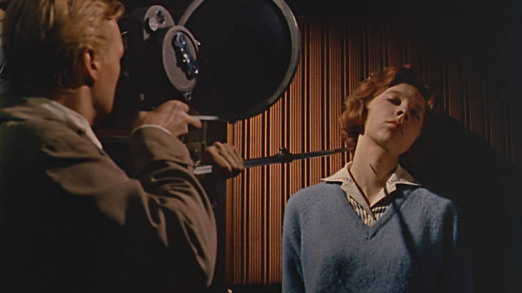 A still from the film Peeping Tom of a man holding a camera with a knife attached about to kill a woman