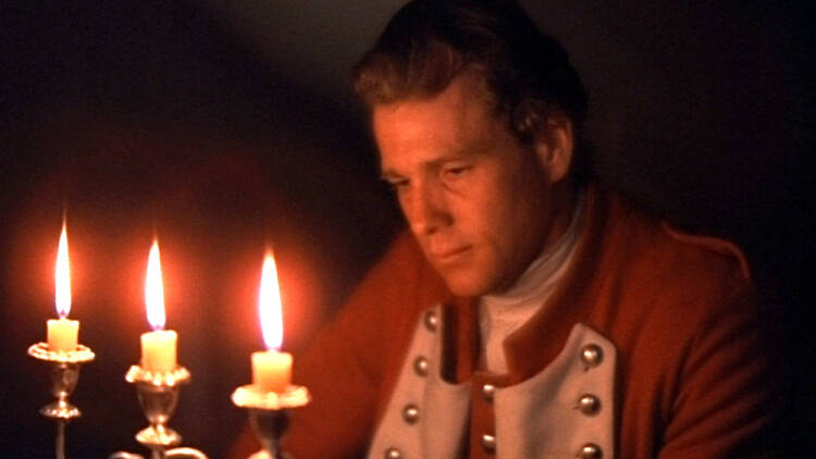 A still from the film Barry Lyndon of a man in period dress looking into the flames of candles in a candelabra 