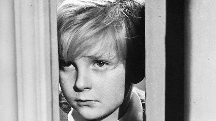A still from the black and white film The Fallen Idol of a young boy peering out from behind a door