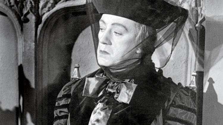 A still from the black and white film Kind Hearts and Coronets of a man dressed as a woman in a period costume