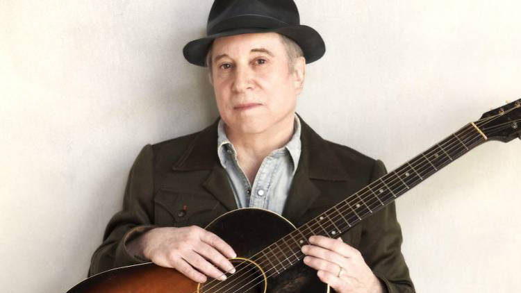 A photograph of Paul Simon holding an acoustic guitar